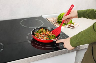 Kızartma tavasında taze sebze ve spatula karıştıran kadın, yakın plan.