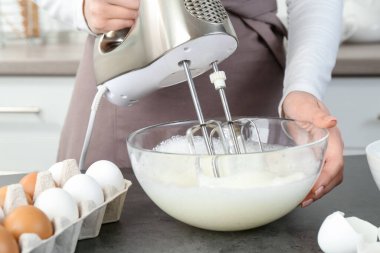 Mutfaktaki gri masada yumurta beyazını mikserle döven kadın, yakın plan.