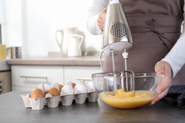 Mutfaktaki gri masada yumurta çırpan kadın, yakın plan.