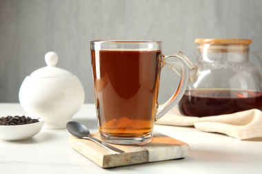 Cam fincanda lezzetli çay ve beyaz masada çay kaşığı gri arka planda, yakın plan