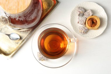 Cam fincanda lezzetli çay, çaydanlık ve Türk tatlıları beyaz masada, düz yerde.