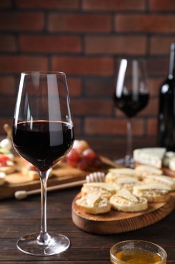 Bir kadeh kırmızı şarap ve ahşap masada lezzetli bruschetalar, tuğla duvara karşı, yakın plan.