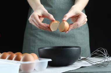 Gri ahşap masada siyah arka planda yumurta kıran kadın, yakın plan.