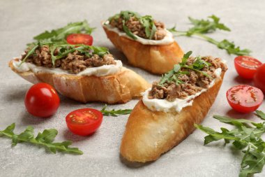 Ton balıklı lezzetli bruschettalar, domatesler ve roka gri masada, yakın plan.