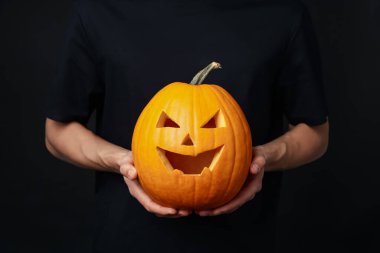 Cadılar Bayramı kutlaması. Siyah arka planda oyulmuş ürkütücü yüzlü balkabağı tutan adam, yakın plan.