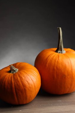 Cadılar Bayramı için iki balkabağı ahşap masada, siyah eğimli arka plana karşı, yakın plan.