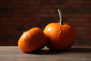 Cadılar Bayramı için iki balkabağı ahşap masada, tuğla duvara karşı, yakın plan.