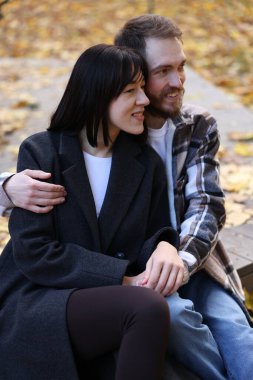 Sonbahar parkında el ele tutuşan gülümseyen çift.