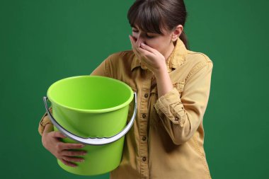 Yeşil arka planda bulantı çeken kovalı genç bir kadın.