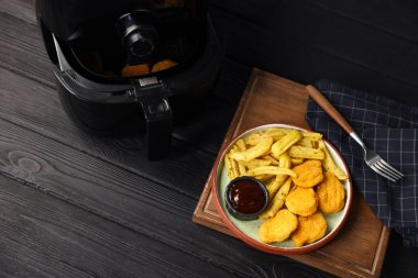 Kızarmış patates kızartması, tavuk nugget, sos ve tavuklu kızartma makinesi siyah ahşap masada, düz yatıyordu. Metin için boşluk