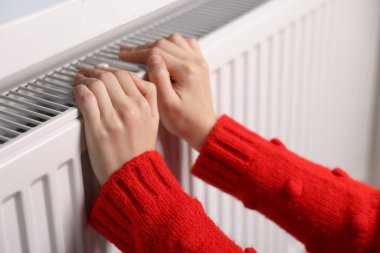 Kadın ellerini radyatörün yanında ısıtıyor, yakın plan.