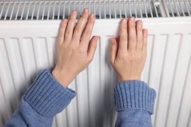 Kadın ellerini radyatörün yanında ısıtıyor, yakın plan.
