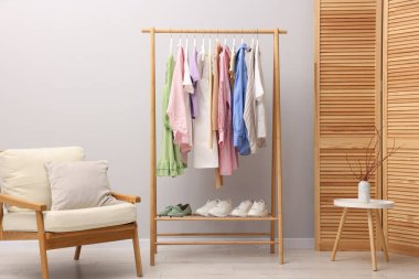 Askıda asılı farklı şık kıyafetler, ayakkabılar ve açık duvarın yanındaki koltuk.