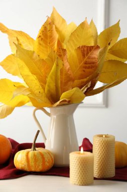 Sonbahar atmosferi. Güzel kuru yapraklı vazo, balkabağı ve yanan mumlar beyaz ahşap masada, yakın plan.