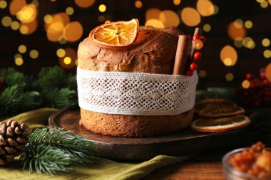 Noel yemeği. Lezzetli Panettone pastası, malzemeler ve ahşap masanın üzerindeki dekoratif dekor arka planda bulanık ışıklar, yakın plan. Bokeh etkisi