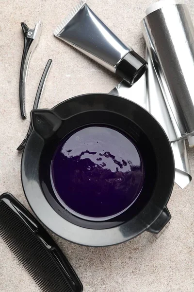 Tabaktaki saç boyama ürünü ve açık gri masada farklı kuaför aletleri.