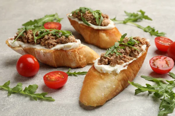 Ton balıklı lezzetli bruschettalar, domatesler ve roka gri masada, yakın plan.