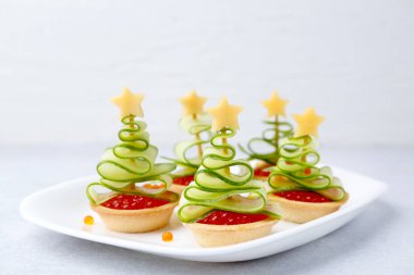 Kırmızı havyar, salatalık ve peynirden yapılmış Noel ağacı şekilli tartlar beyaz masada, yakın plan.