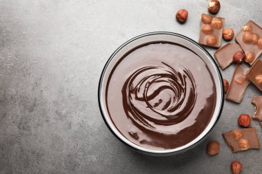 Erimiş çikolata kasede, parçalar ve fındıklar gri masada, düz yerde. Metin için boşluk