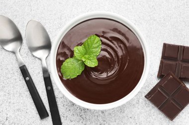 Erimiş çikolata kasede nane, parçalar ve kaşıklar açık gri masada, düz yatıyordu.