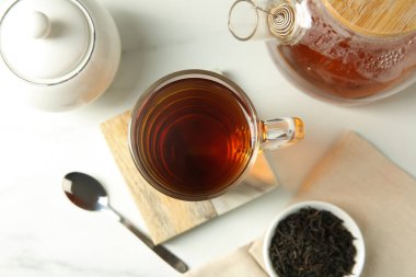 Cam bardaktaki lezzetli çay, kuru yapraklar, çaydanlık, şeker kasesi ve çay kaşığı beyaz masada, düz konaklama