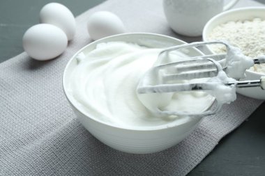 Kırbaçlanmış beyazlar kasede, mikserde, un ve yumurtalar gri ahşap masada, yakın plan