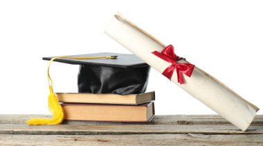 Diploma, kitap ve mezuniyet şapkası beyaz arka plana karşı ahşap masada.