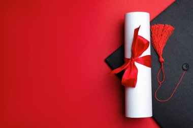 Kırmızı arka planda diploma ve mezuniyet şapkası, üst manzara. Metin için boşluk