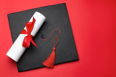 Kırmızı arka planda diploma ve mezuniyet şapkası, üst manzara. Metin için boşluk