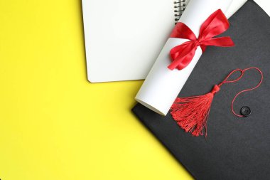 Diploma, mezuniyet şapkası ve sarı arka planda defter, düz yatış. Metin için boşluk