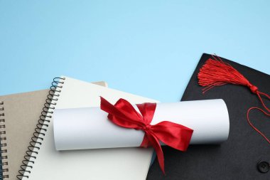 Diploma, mezuniyet şapkası ve açık mavi arkaplan üzerine not defterleri, metin için boşluk