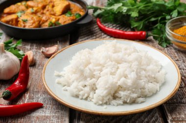 Pişmiş pirinç, tavuk tikka masala ve ahşap masada baharatlar, yakın plan.