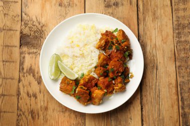 Pirinçli, maydanozlu ve ahşap masadaki limonlu leziz tavuk tikka masala..