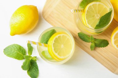 Taze limonata bardaklarda, limonlarda ve nane şekerleri beyaz masada, düz yerde.