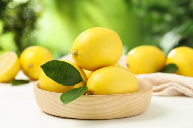 Beyaz ahşap masa üzerinde yeşil yapraklı taze limonlar, yakın plan.