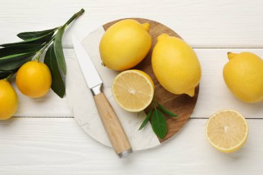 Yeşil yapraklı taze limonlar ve beyaz ahşap masa üzerinde bıçak, düz yatıyordu.