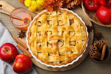 Lezzetli ev yapımı turta, taze elmalar, bal ve çiçekler ahşap masada, düz uzanmış.