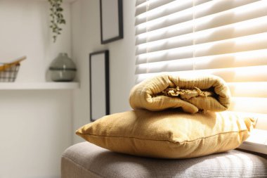 Yumuşak yastık ve battaniye pencerenin yanındaki puf üzerinde, yakın çekim. Metin için boşluk