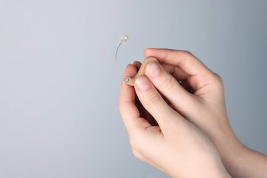 Açık gri arka planda işitme cihazı olan bir kadın, yakın plan. Metin için boşluk