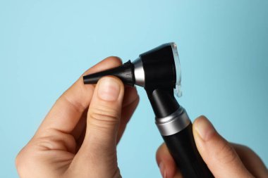 Duyma testi. Açık mavi arka planda otoskop ve kulak spekulumu olan kadın, yakın plan.