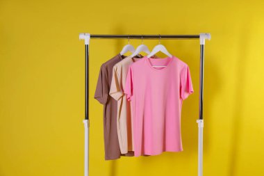 Farklı kadın kıyafetleri sarı arka planda asılı duruyor.