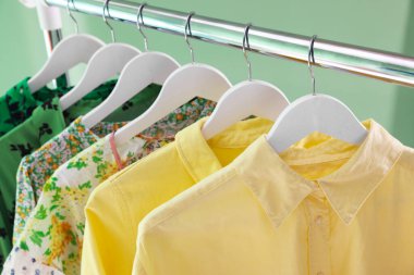 Farklı kadın kıyafetleri yeşil arka planda asılı, yakın plan.