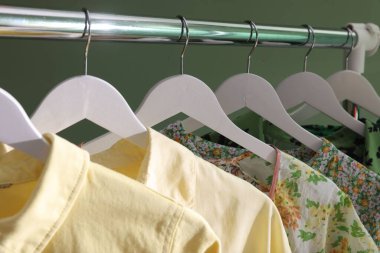 Farklı kadın kıyafetleri yeşil arka planda asılı, yakın plan.