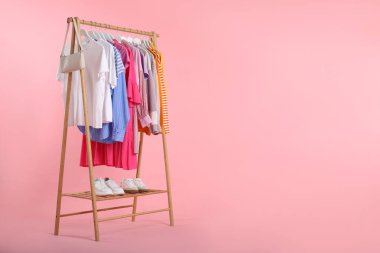 Rafta asılı farklı giysiler, çanta ve ayakkabılar pembe arka plana karşı, metin için boşluk