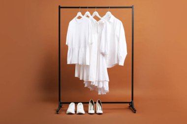 Farklı elbiseler askıda asılı ve ayakkabılar kahverengi arka planda