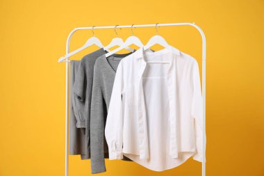 Farklı giysiler turuncu arka planda asılı duruyor.