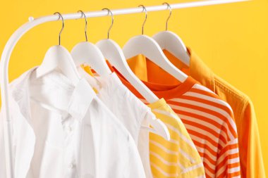 Farklı giysiler turuncu arka planda asılı, yakın plan.