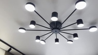 Aydınlatılmış bir avize ve odanın beyaz tavanında raylı aydınlatma.