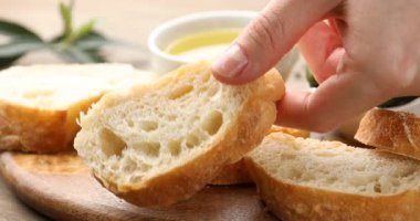 Ciabatta dilimleyen bir kadın, ahşap masada yağın içine, yakın plan.