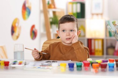 Beyaz masa içinde fırçayla çizim yapan sevimli küçük çocuk.